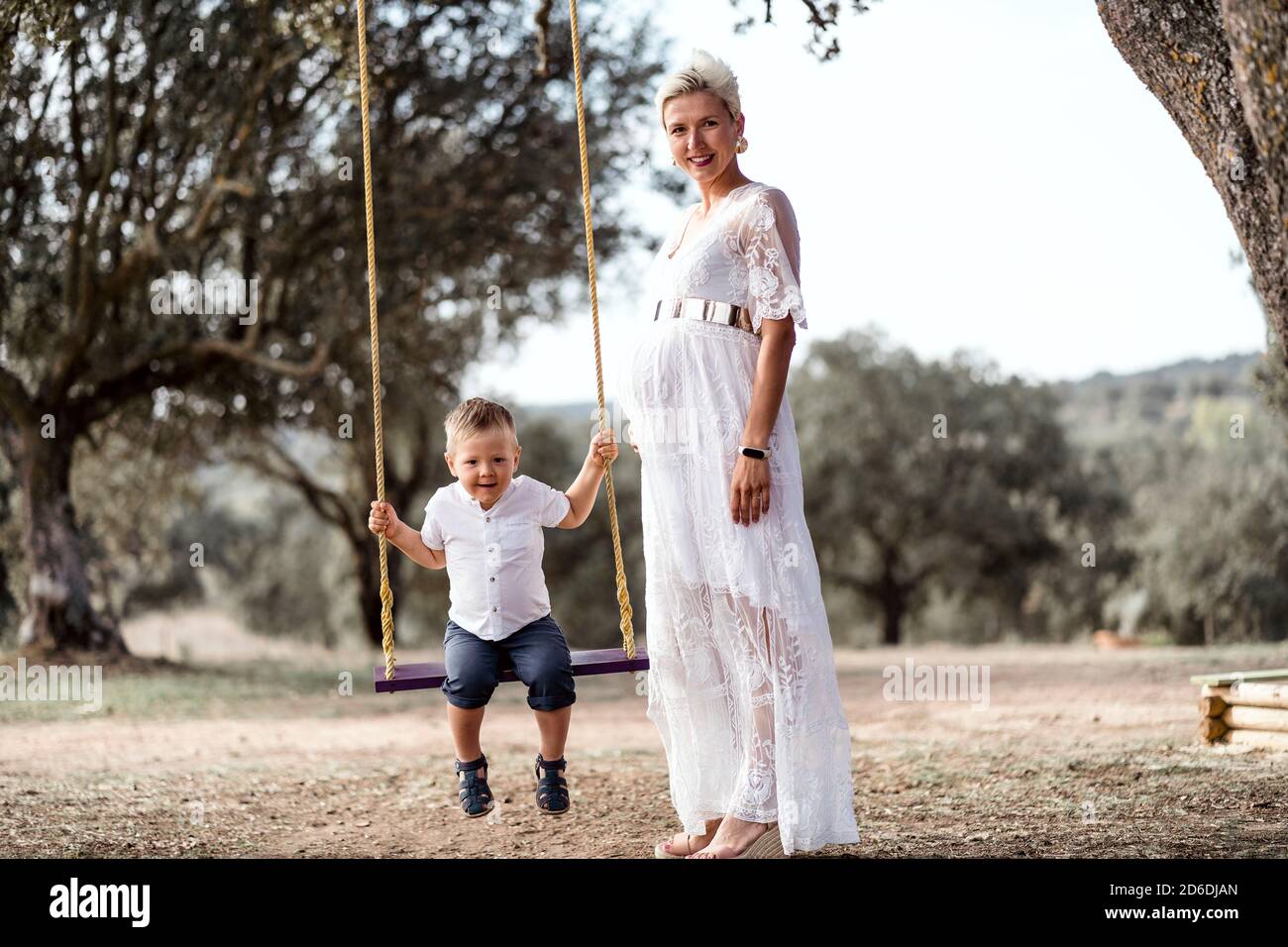 Pregnant woman having fun with her toddler son on the swing in the park Stock Photo