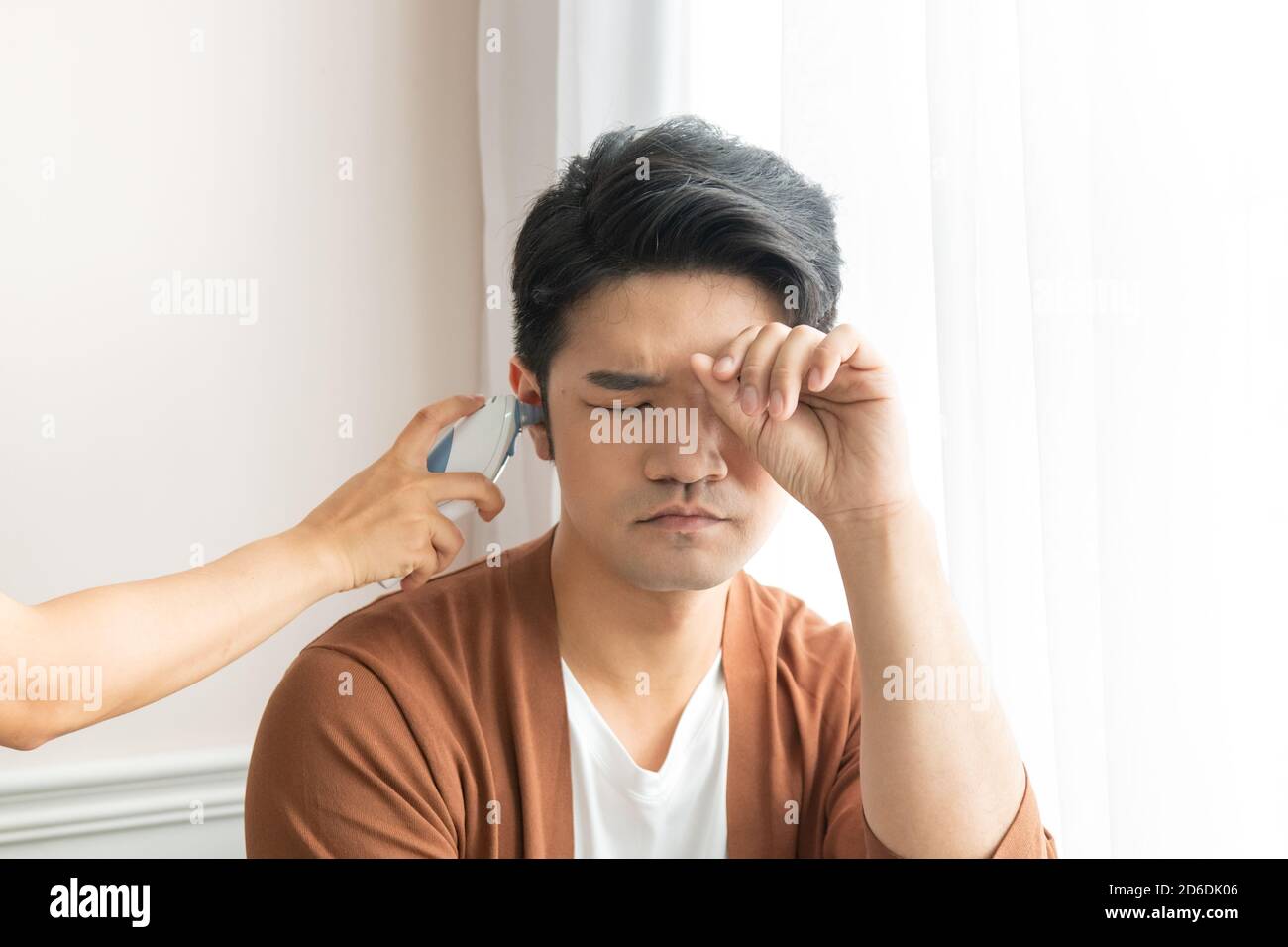 The man with fever is using an ear thermometer to measure his