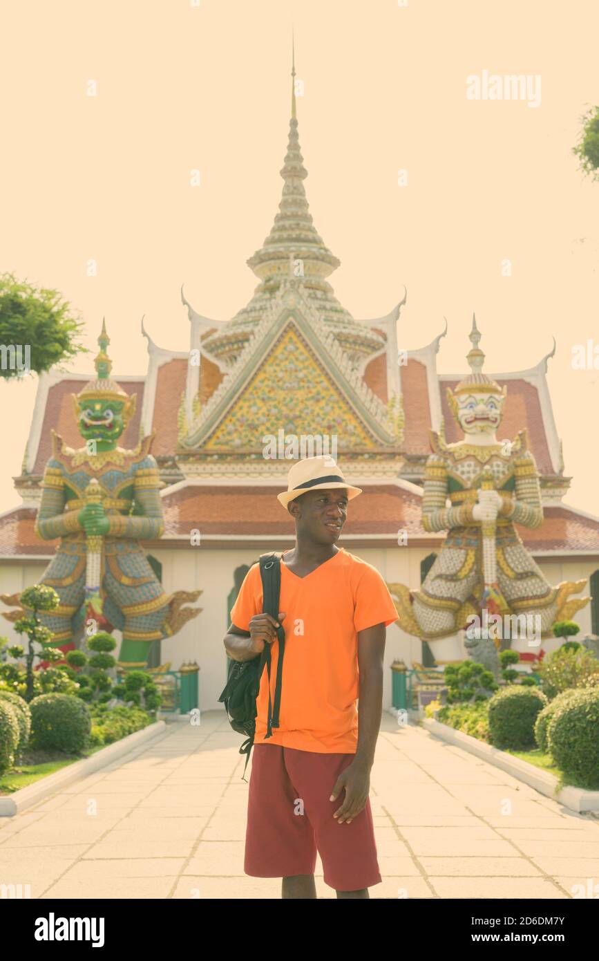 Young black African tourist man thinking while holding backpack and standing outside of Wat Arun temple in Bangkok Thailand Stock Photo