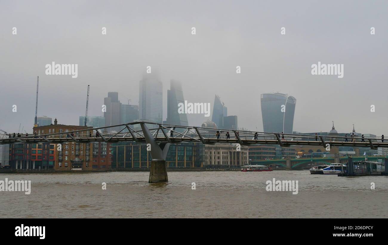 People crossing a modern bridge spanning Thames River in London, UK with skyline in background that vanishes in the autumn mist. Stock Photo
