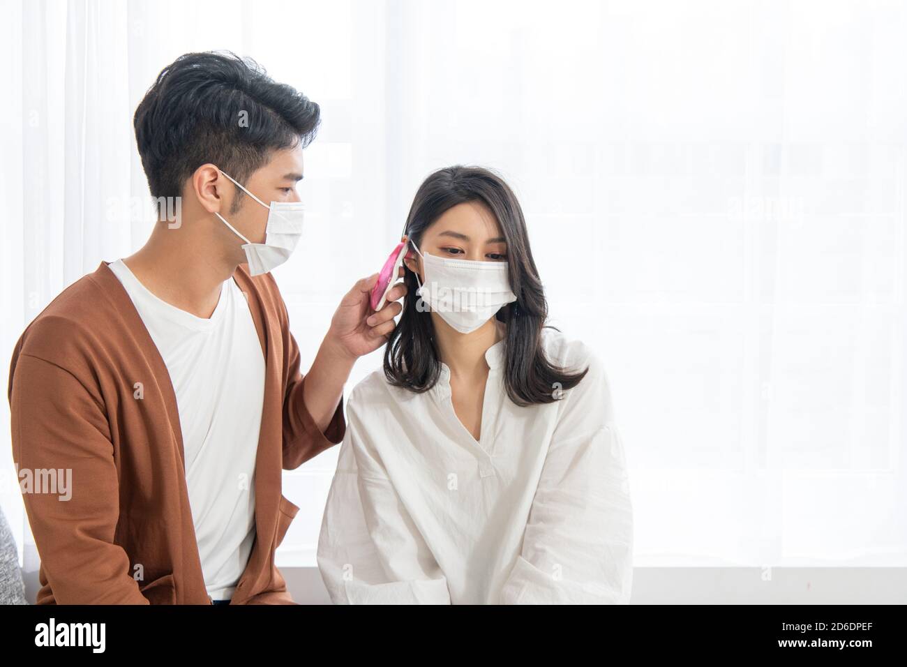 A man takes temperature for her wife with ear thermometer at home(how
