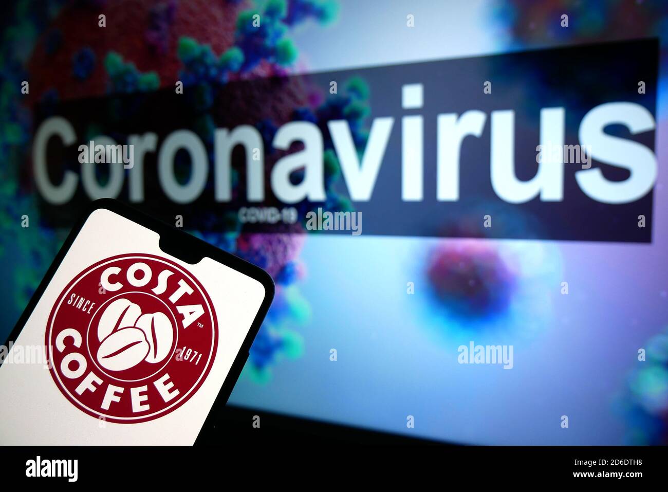 The Costa Coffee logo seen displayed on a mobile phone with an illustrative model of the Coronavirus displayed on a monitor in the background. Stock Photo