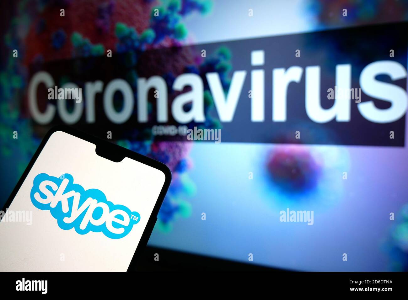 The Skype logo seen displayed on a mobile phone with an illustrative model of the Coronavirus displayed on a monitor in the background. Stock Photo