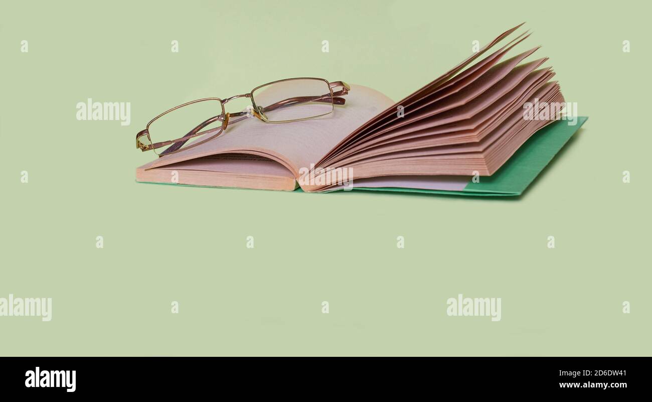 The glasses are lying on an open book on a solid green background Stock Photo