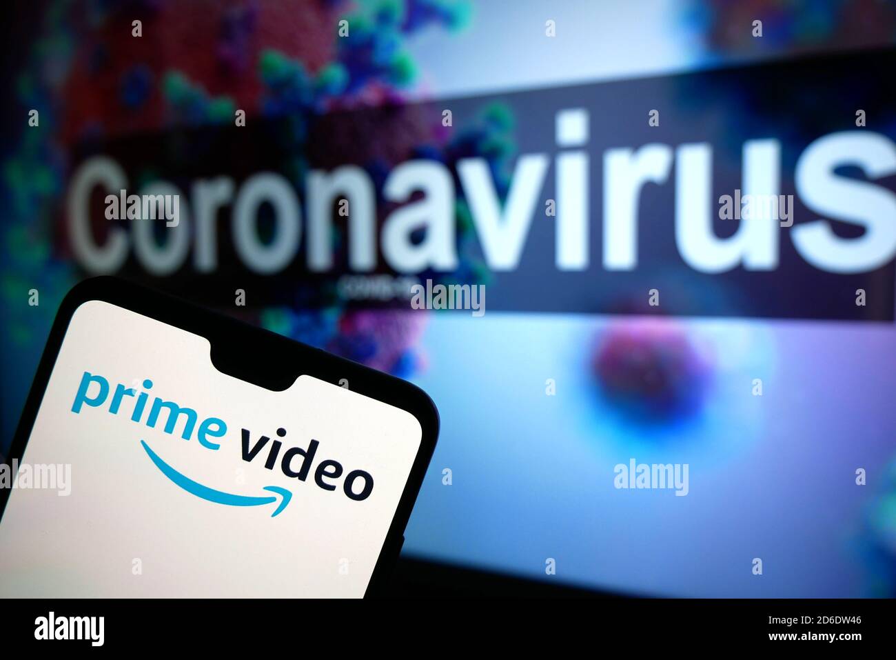 The Amazon Prime Video logo seen displayed on a mobile phone with an illustrative model of the Coronavirus displayed on a monitor in the background. Stock Photo