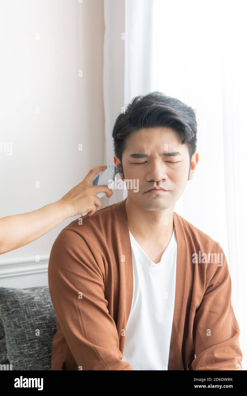 The man with fever is using an ear thermometer to measure his