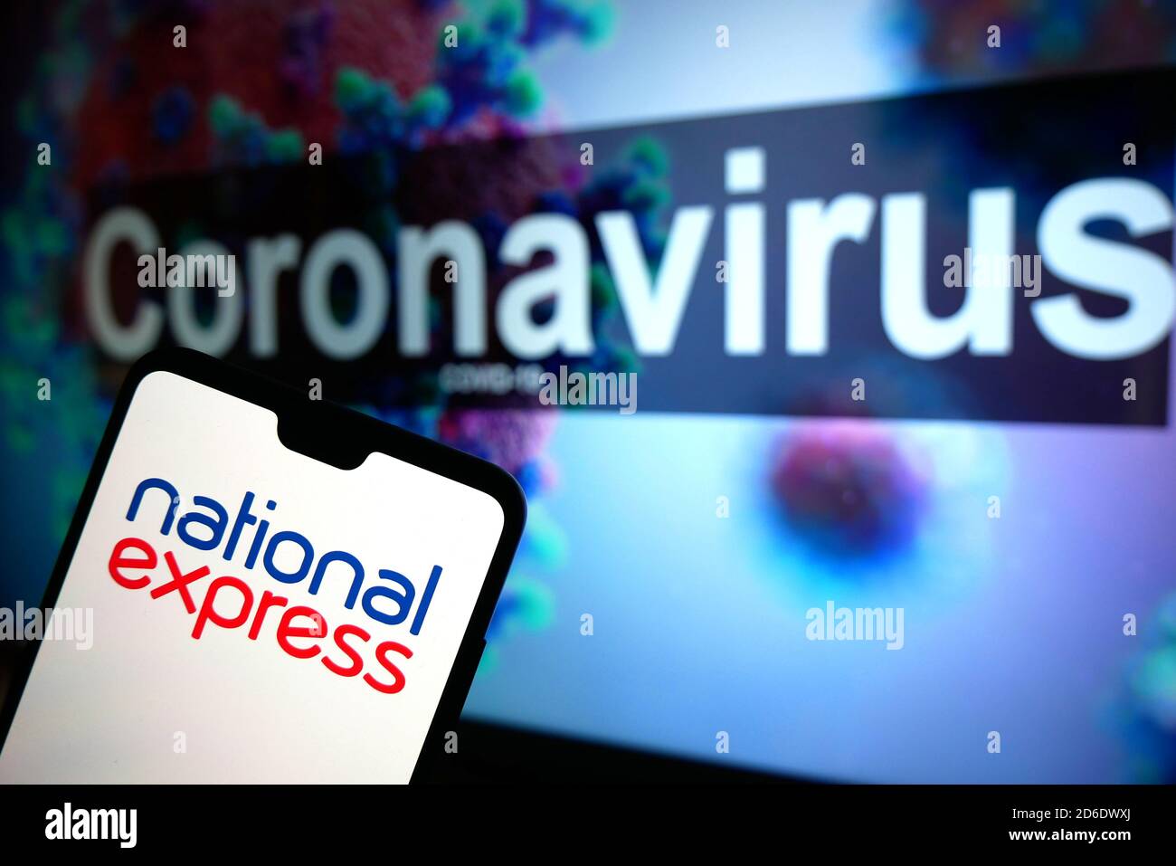 The National Express logo seen displayed on a mobile phone with an illustrative model of the Coronavirus displayed on a monitor in the background. Stock Photo