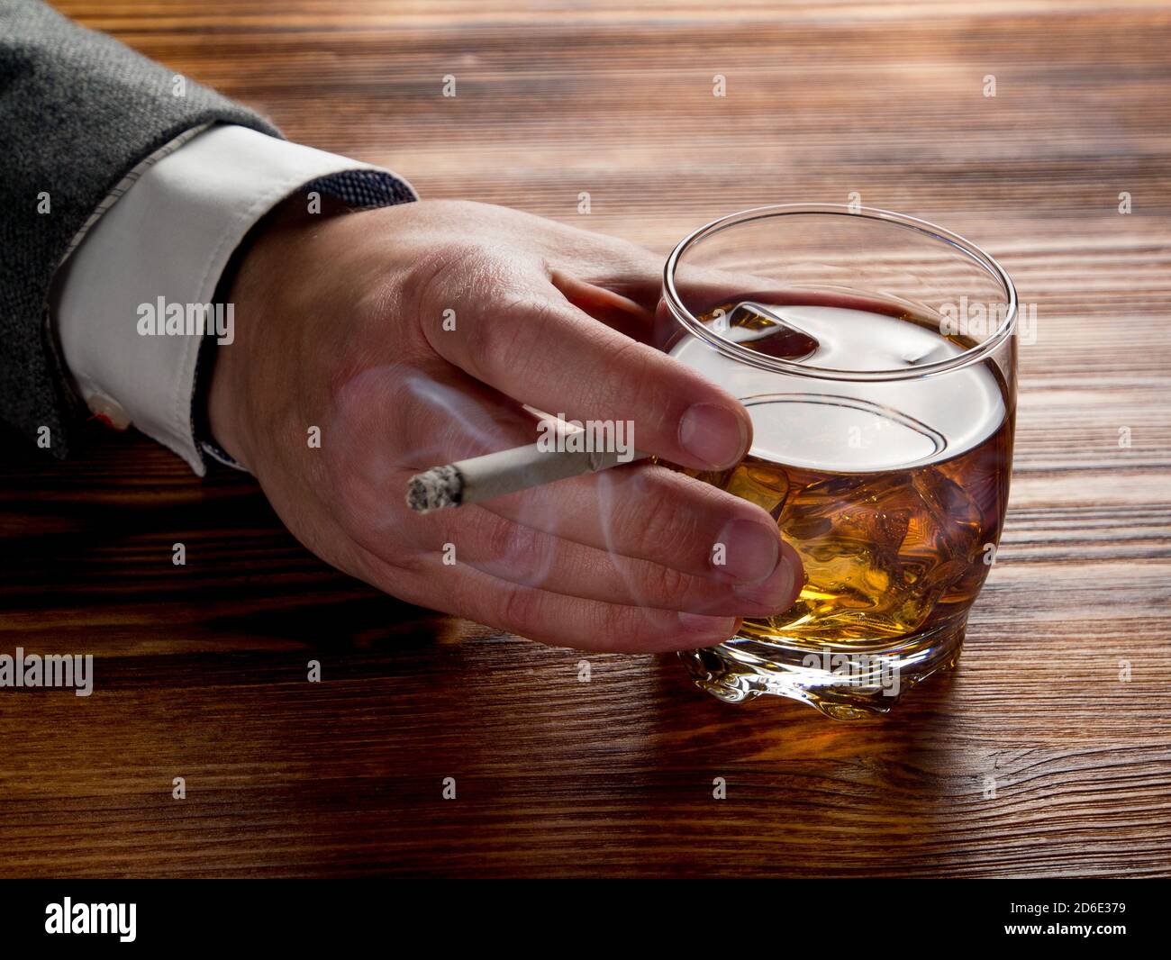 Man's hand holding a glass of whiskey and a smoking cigarette Stock Photo