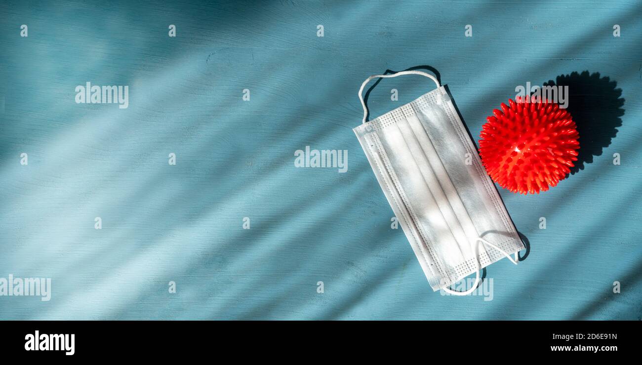 Red plastic corona virus model with protective face mask on blue wooden background. Stock Photo