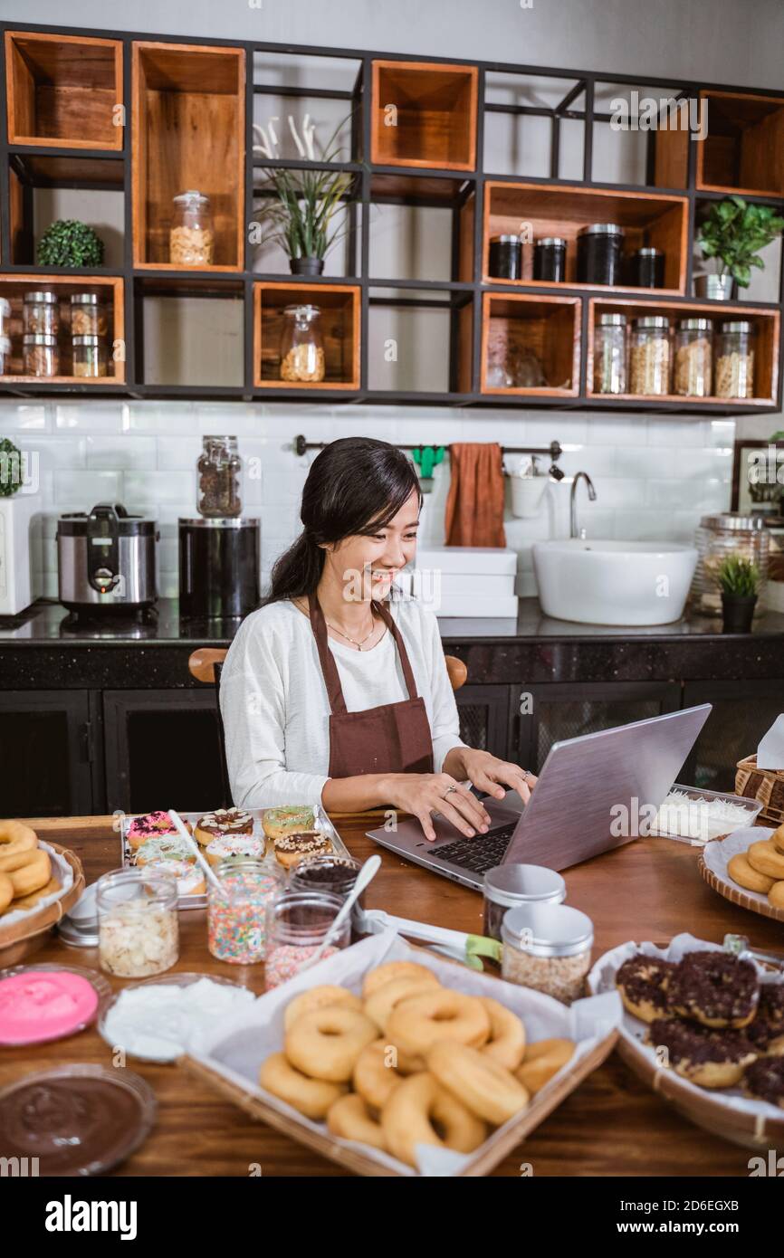 female chef wearing an apron while using a laptop while sitting in the kitchen Stock Photo