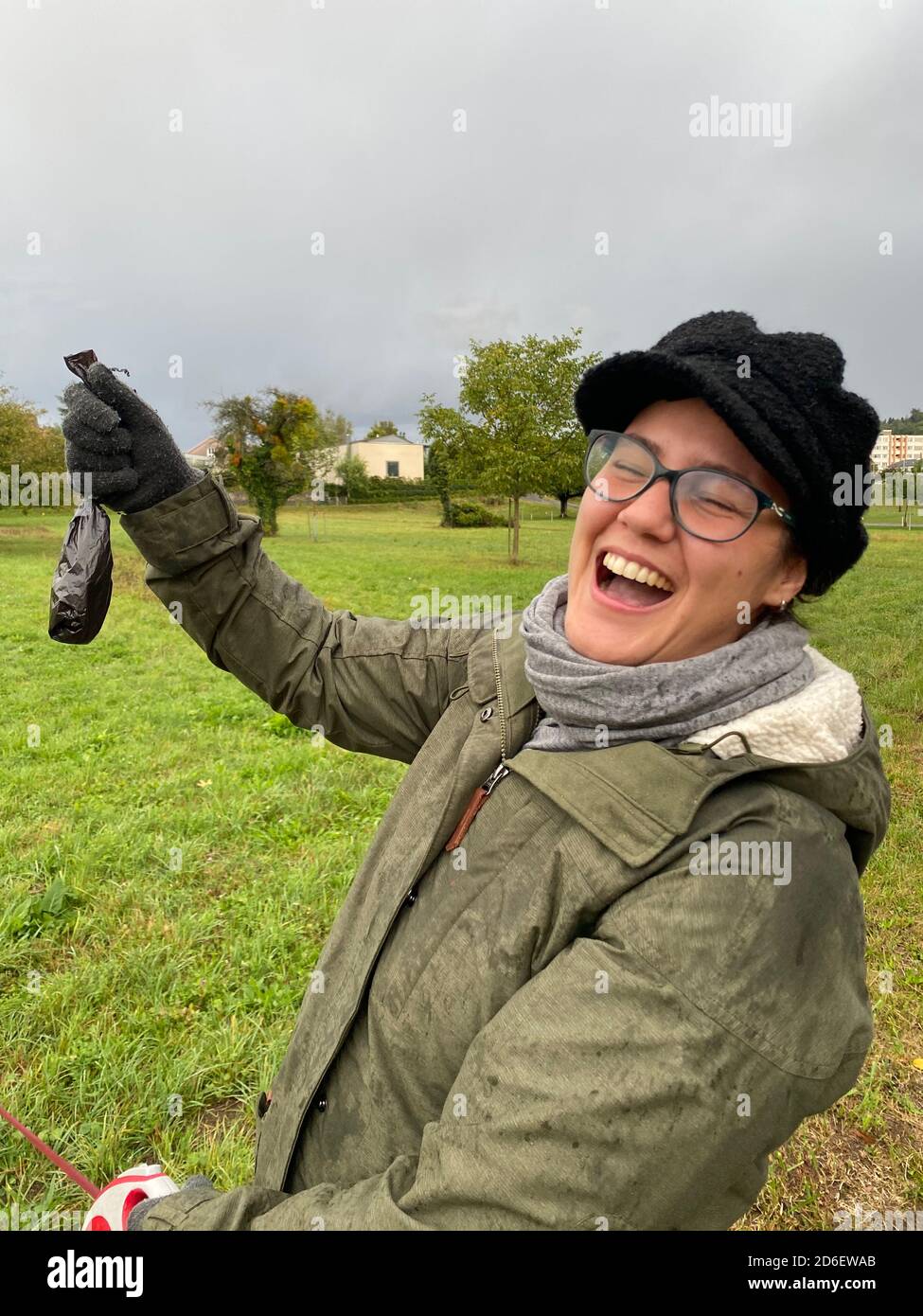 Laughing girl holding feces bag of dog in hand at rainy autumn day. Stock Photo
