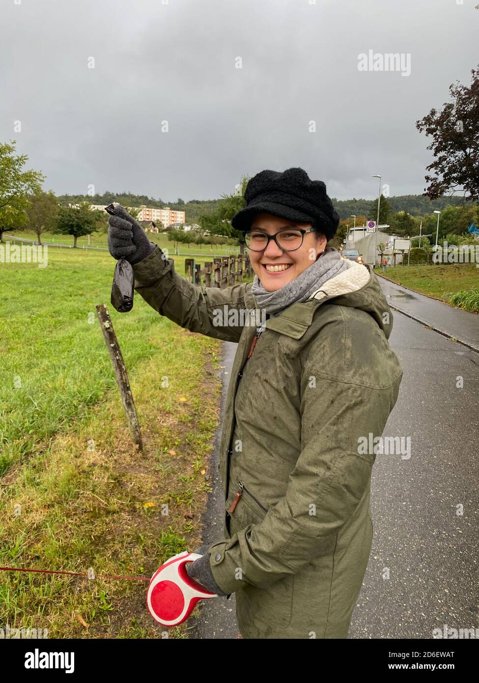 Laughing girl holding feces bag of dog in hand at rainy autumn day. Stock Photo