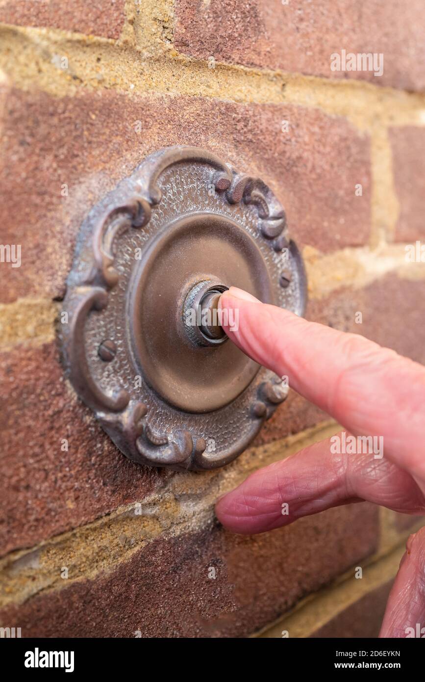 A vintage antique style metal door bell being pushed by the finger of a visitor Stock Photo