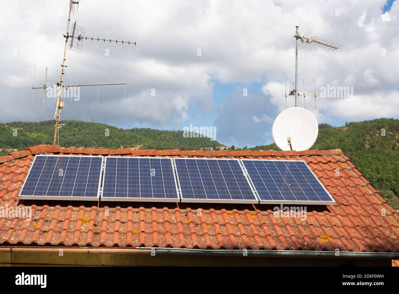 solar panels and antennas on the roof of a house in the countryside. hills covered with woods in the background Stock Photo