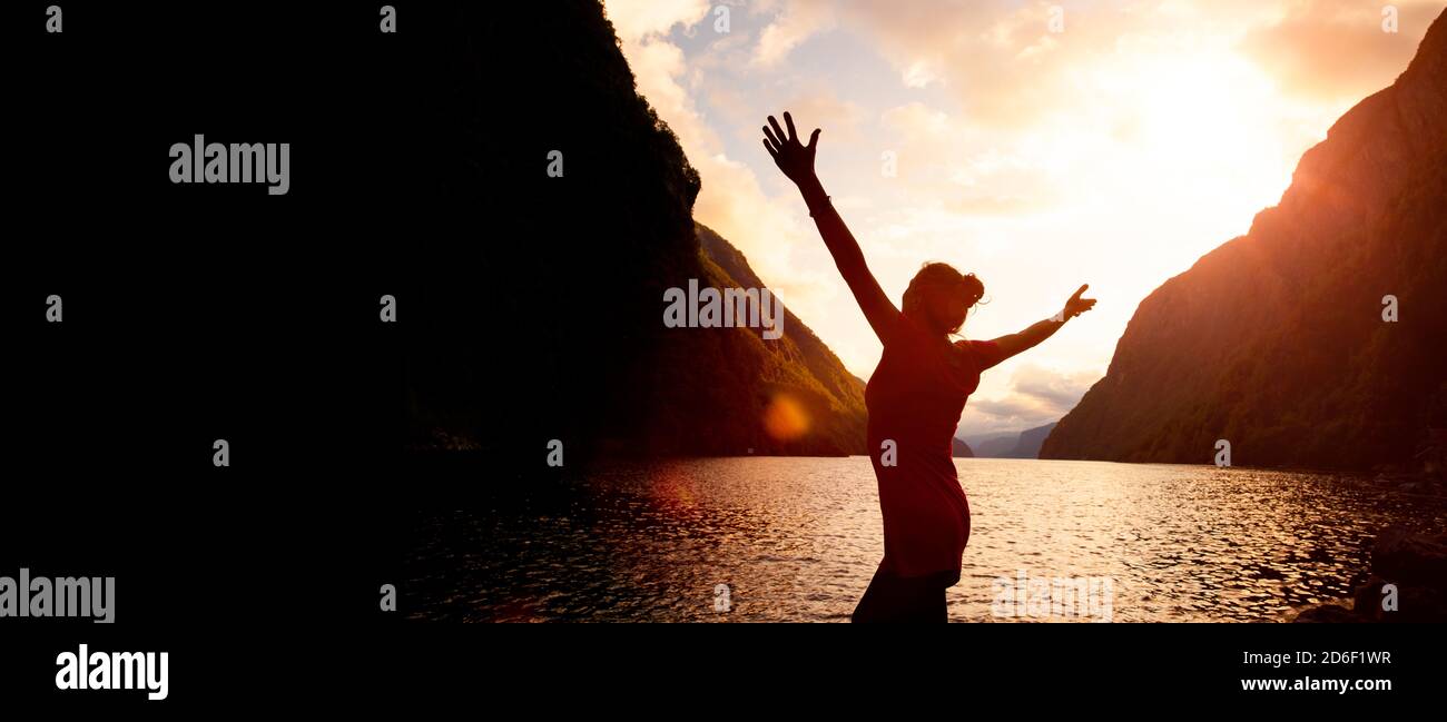 Silhouette of a woman with arms outstretched at sunrise by a lake Stock ...