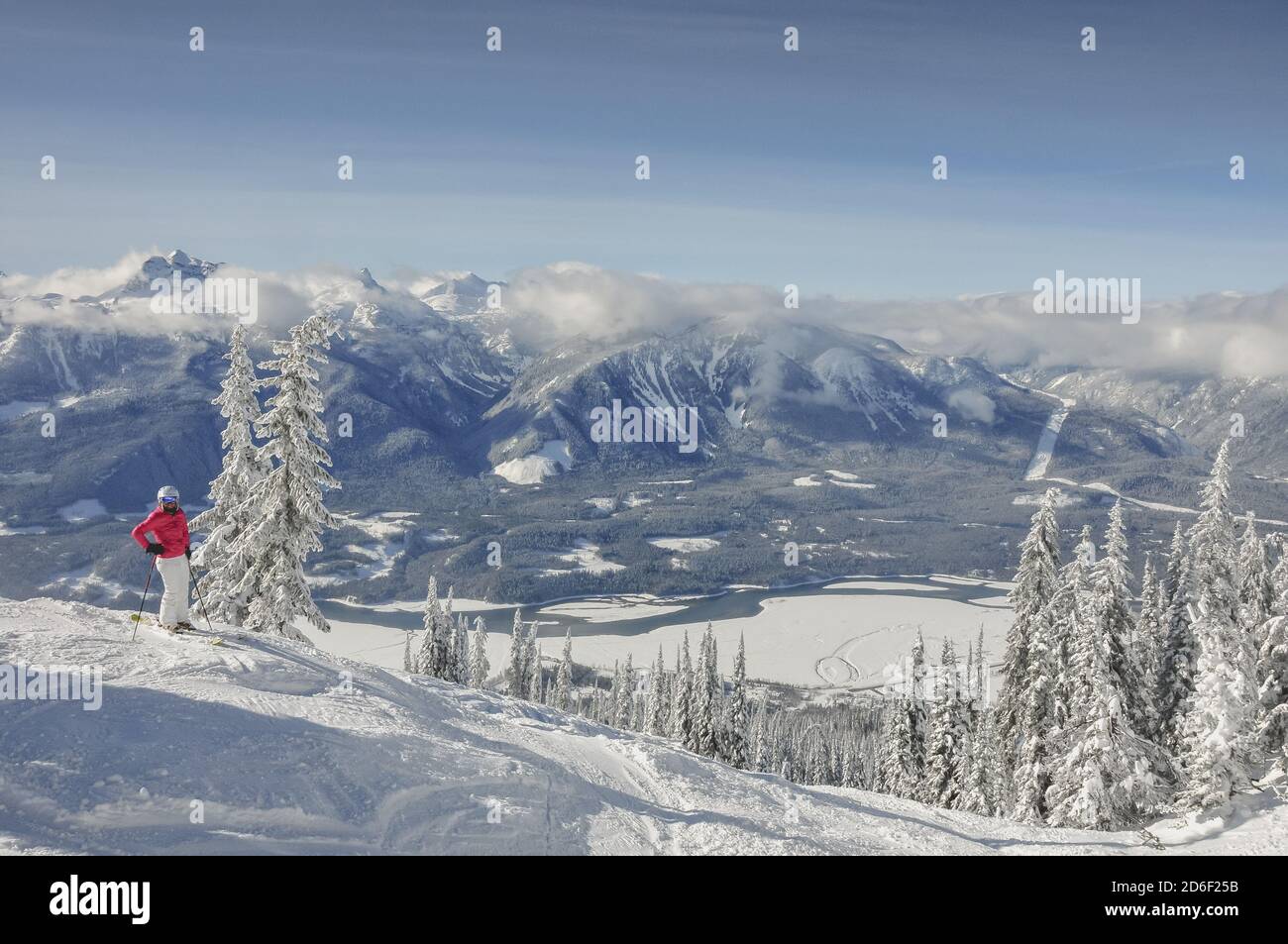 One female skier standing against a backdrop of a majestic winter landscape and snow covered trees. Revelstoke, Canada. Model release. Stock Photo
