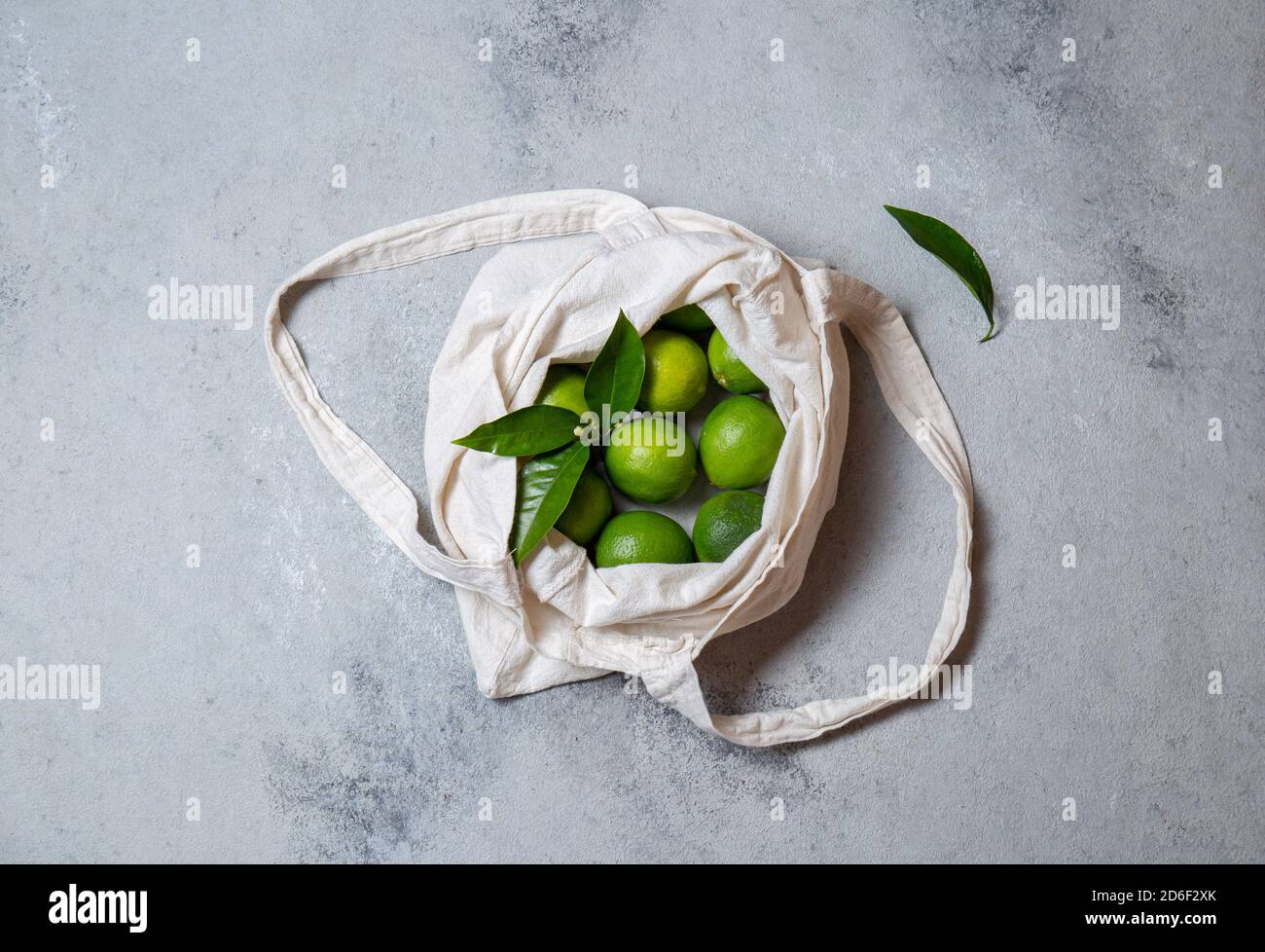 Ripe limes with fresh lime tree leaves in eco linen bag. top view. Stock Photo