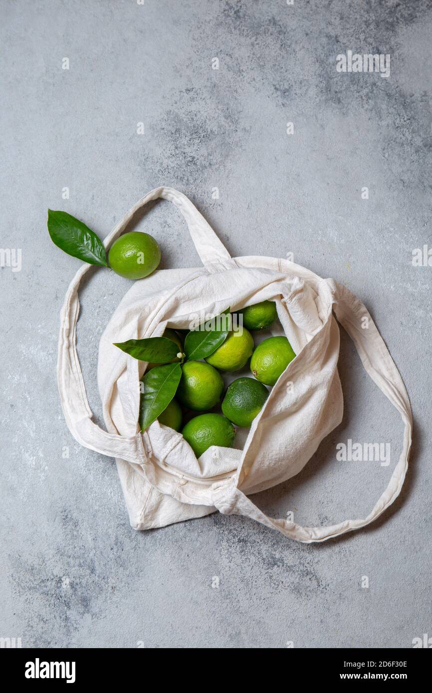 Ripe limes with fresh lime tree leaves in eco linen bag. top view. Stock Photo