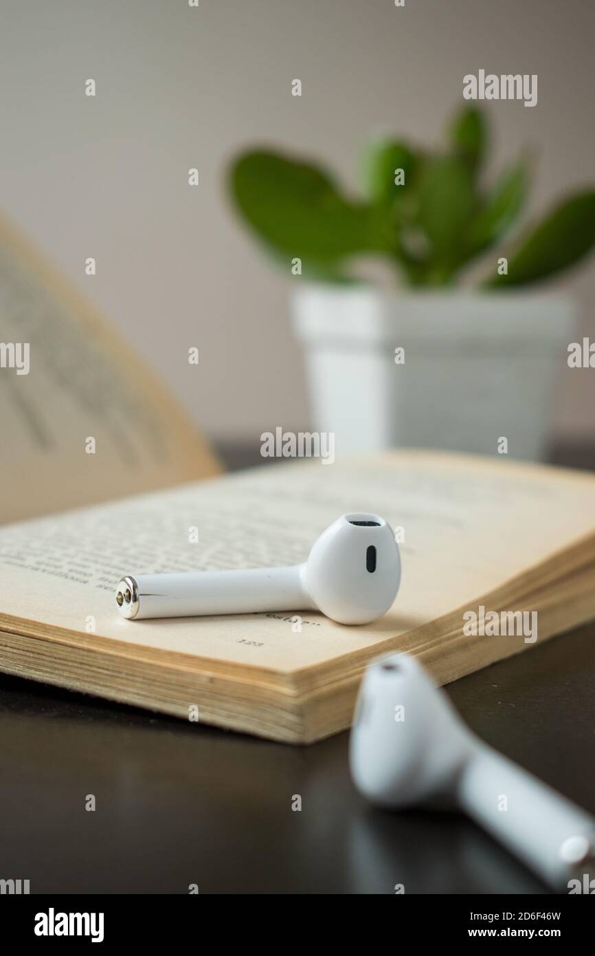 Some modern white earphones on a book  with a little plant on a black wooden table Stock Photo