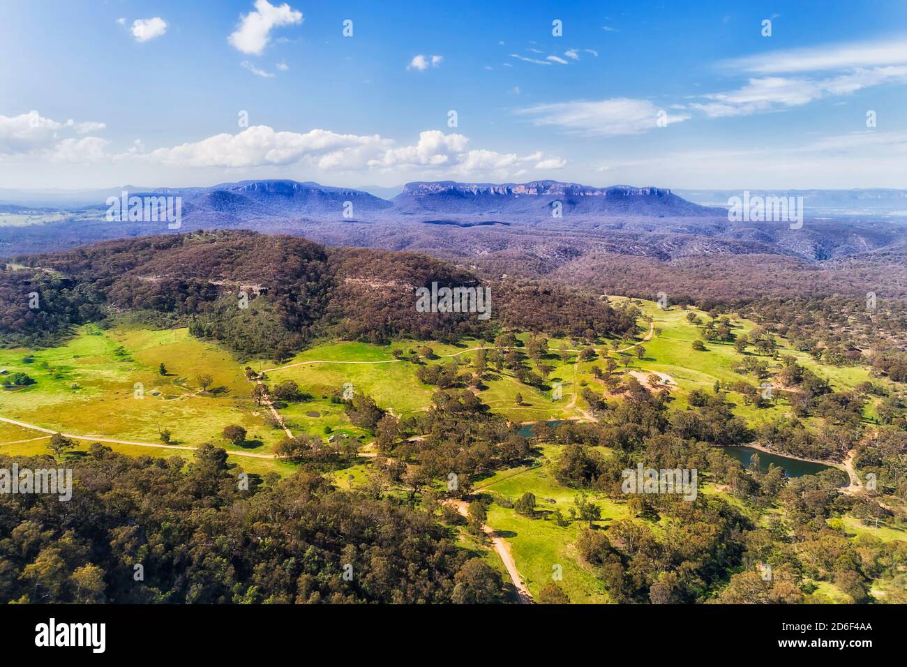 Capertee valley in aerial view above gumtree woods and green pastures between mountain ranges. Stock Photo