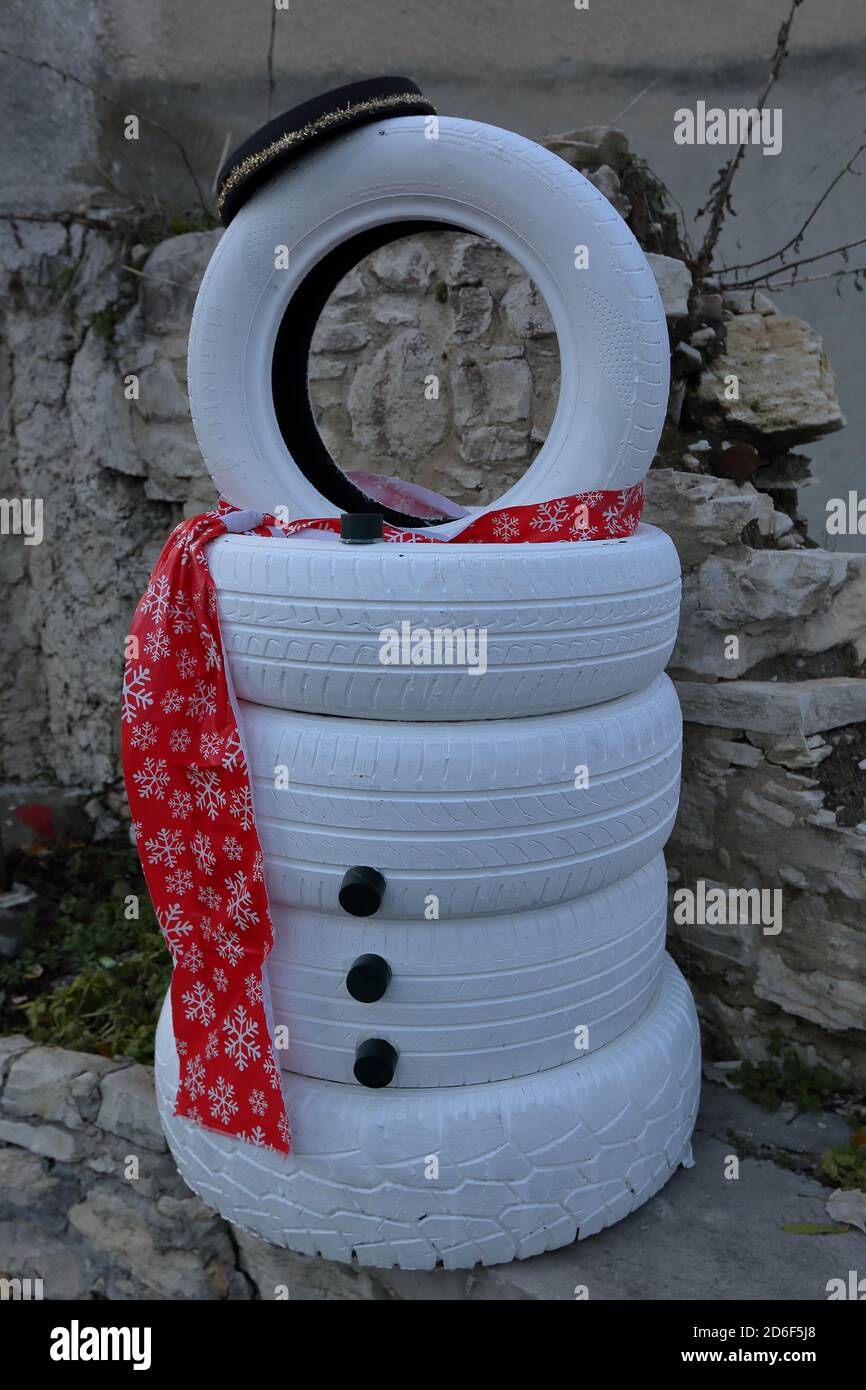 Decorative funny snowman made of car tires painted with white colour, decorated with red scarf and hat. Stock Photo