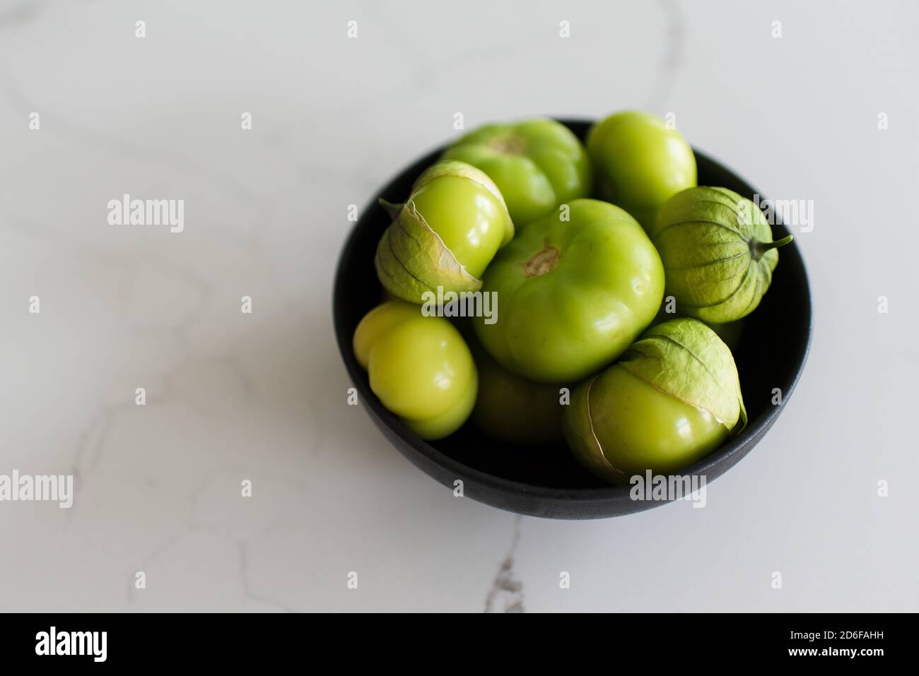 Bowl of fresh green tomatillo fruit on a white quartz counter. Stock Photo