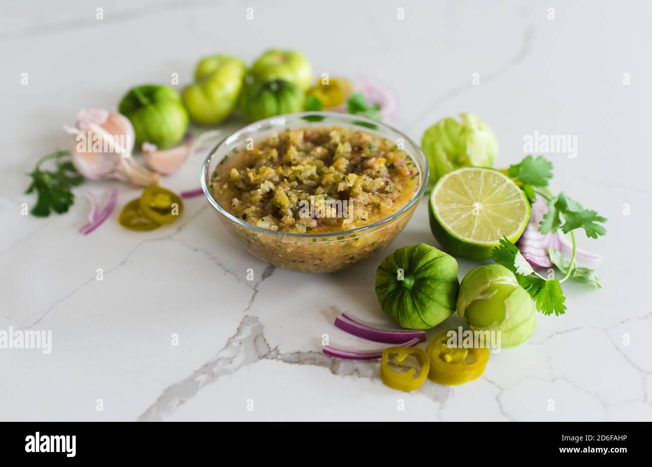 Bowl of tomatillo salsa with it's ingredients on white quartz counter. Stock Photo