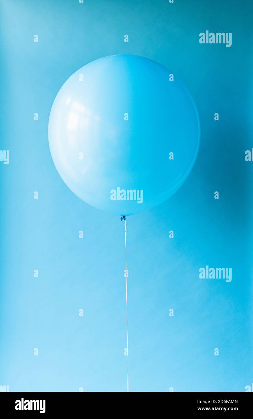 Close up of a blue balloon on a string against a blue backdrop. Stock Photo