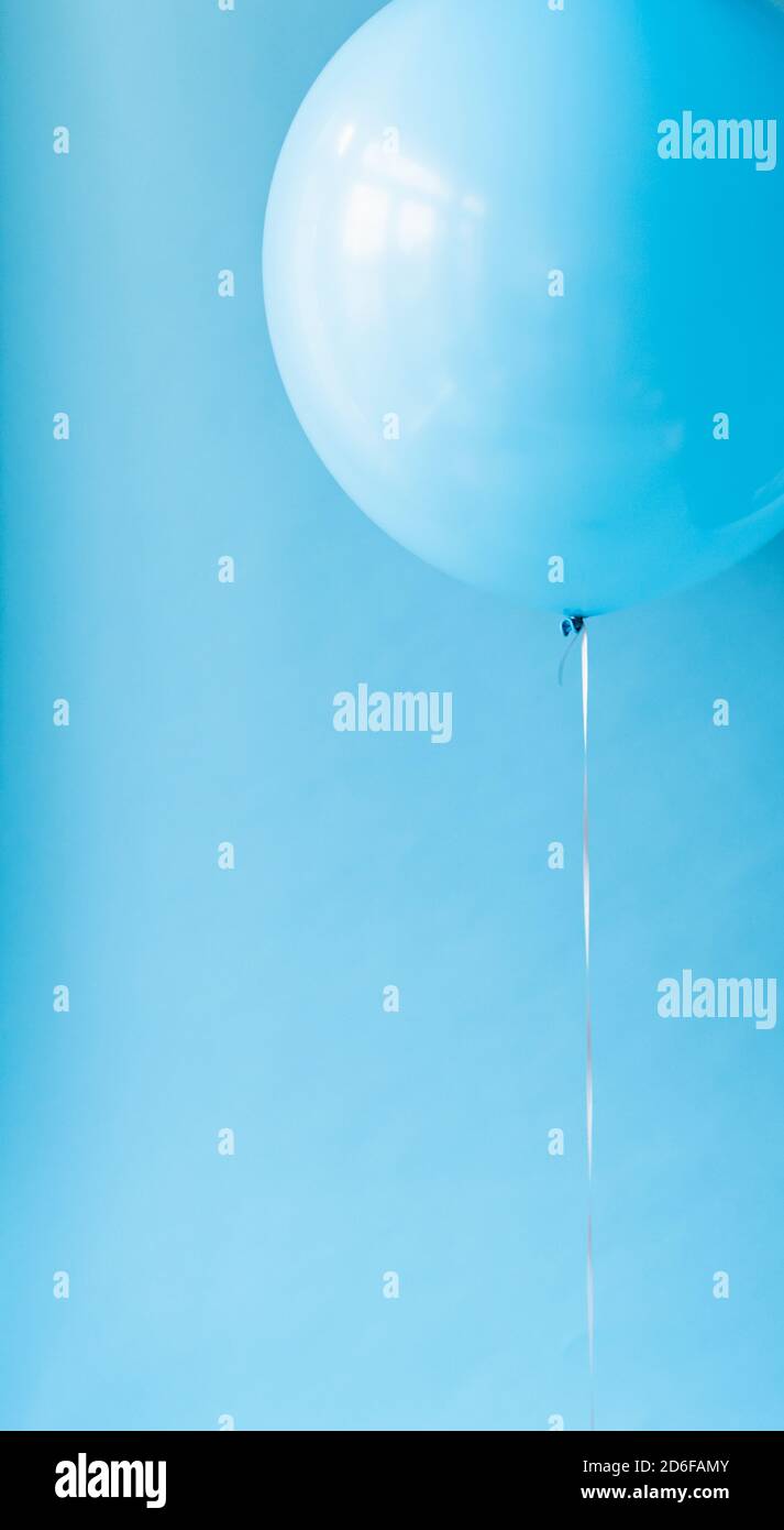 Close up of a blue balloon on a string against a blue backdrop. Stock Photo