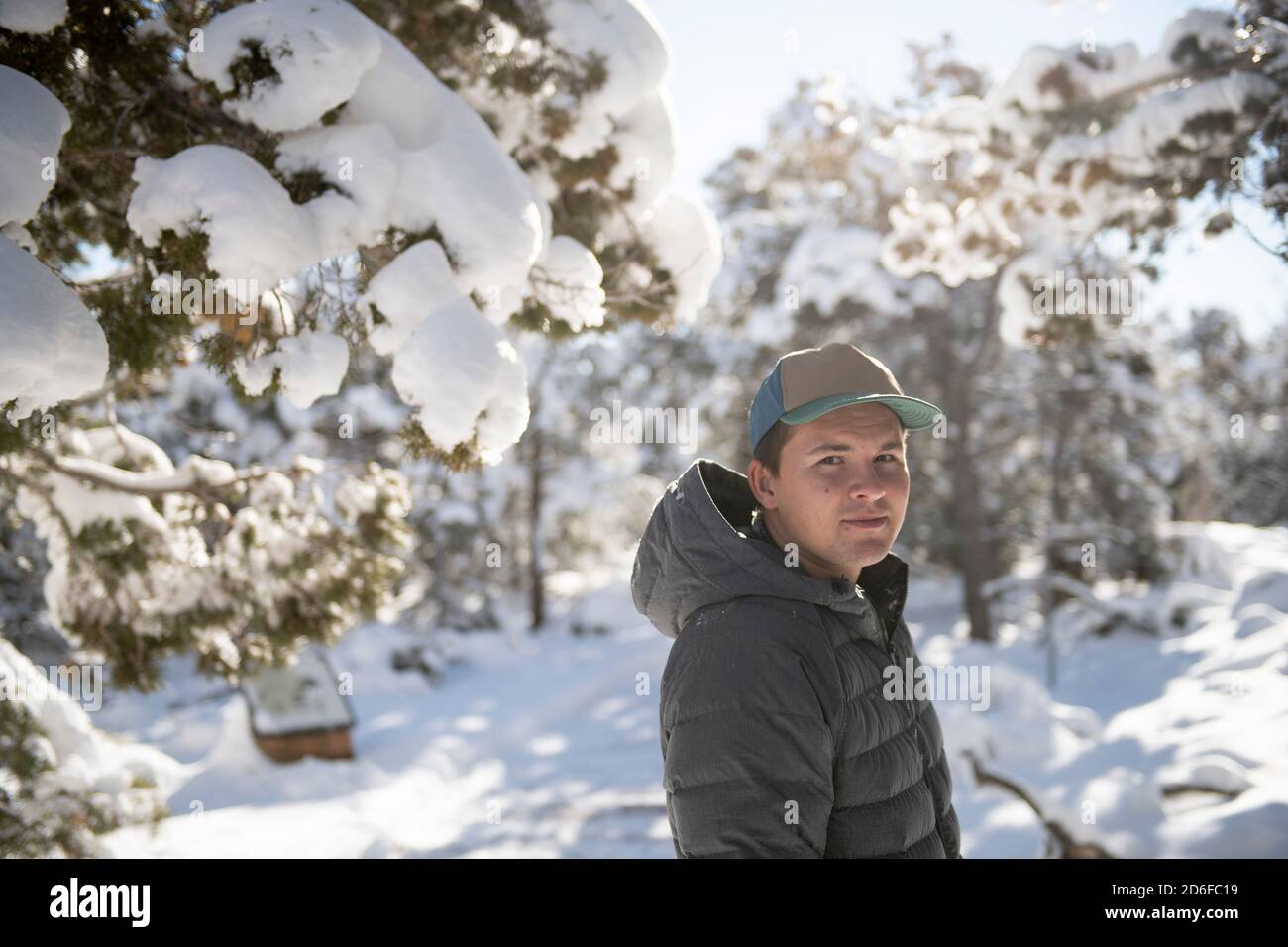 Young adult male smiling at camera in bright snowy pine forest Stock Photo