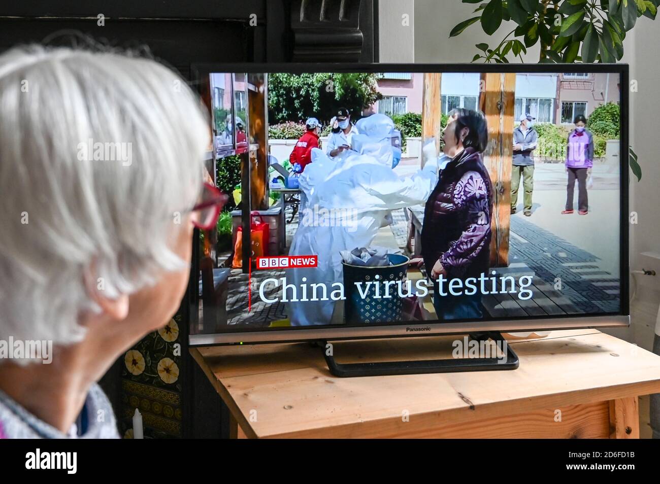 Televised news report of testing Chinese citizens in China for Covid-19,  with 'China virus testing' text, watched by an older viewer. Stock Photo