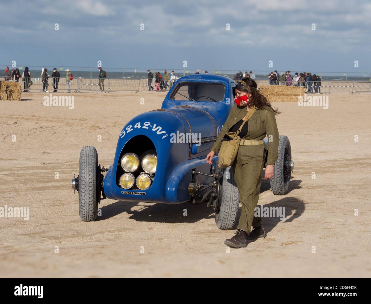 woman in a masthead and retro jumpsuit next to an old Renault car model on a beach in Normandy, France. Normandy Race Beach Stock Photo