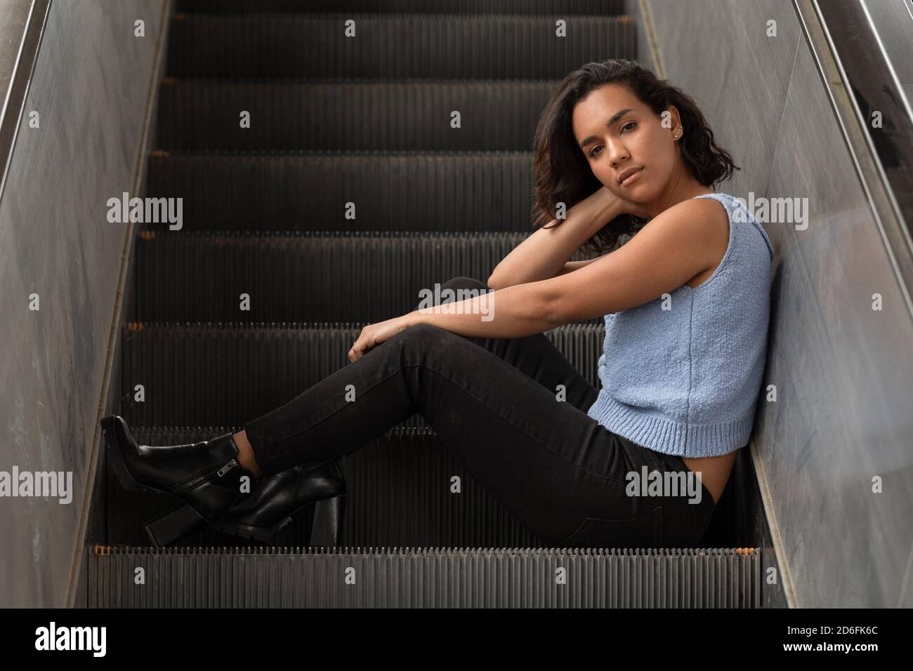young brunette latina girl with short hair with curls, sitting on electric  stands, wearing blue blouse, black pants, casual style Stock Photo - Alamy