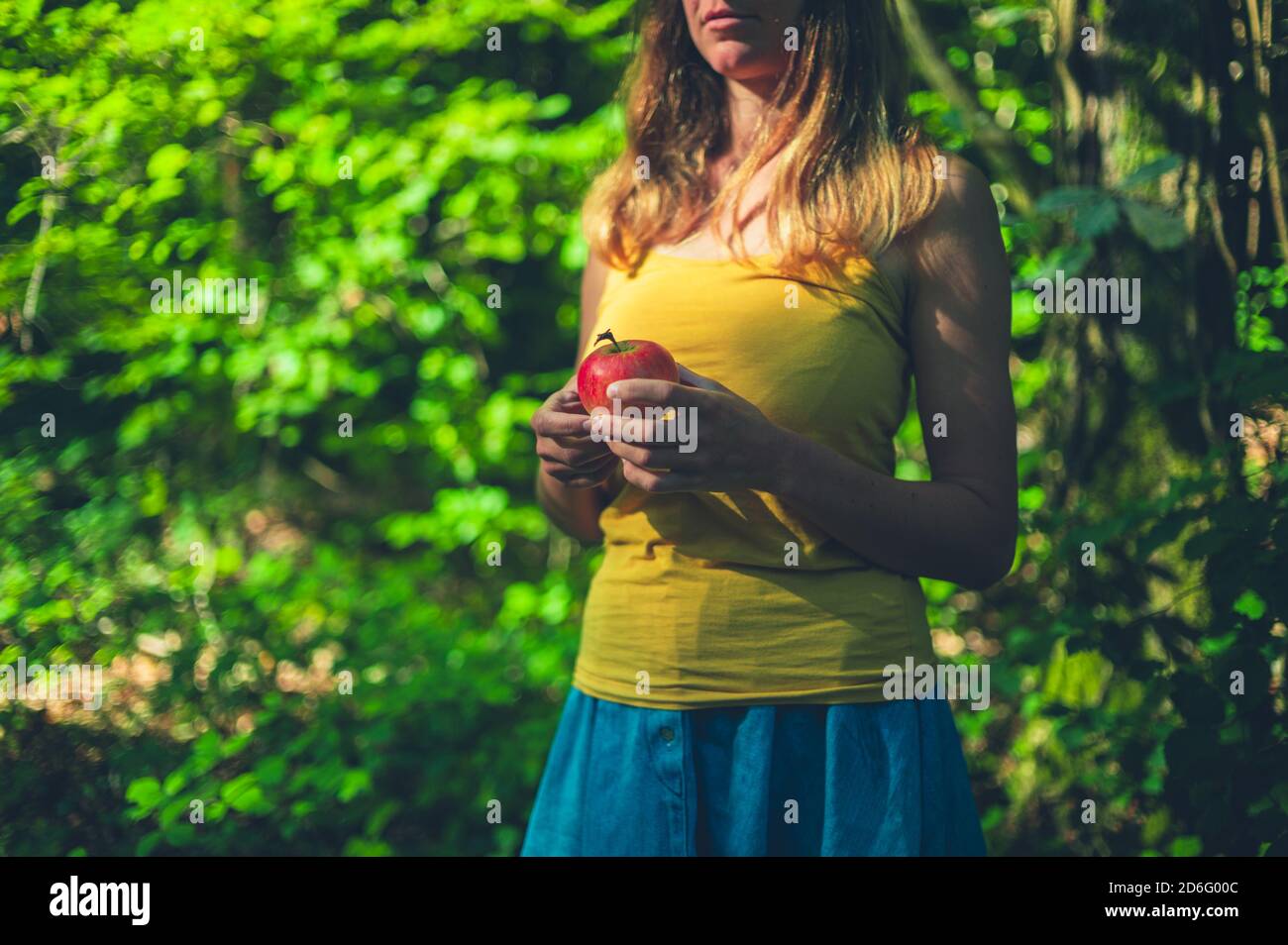 A young woman is standing in the forest with an apple Stock Photo