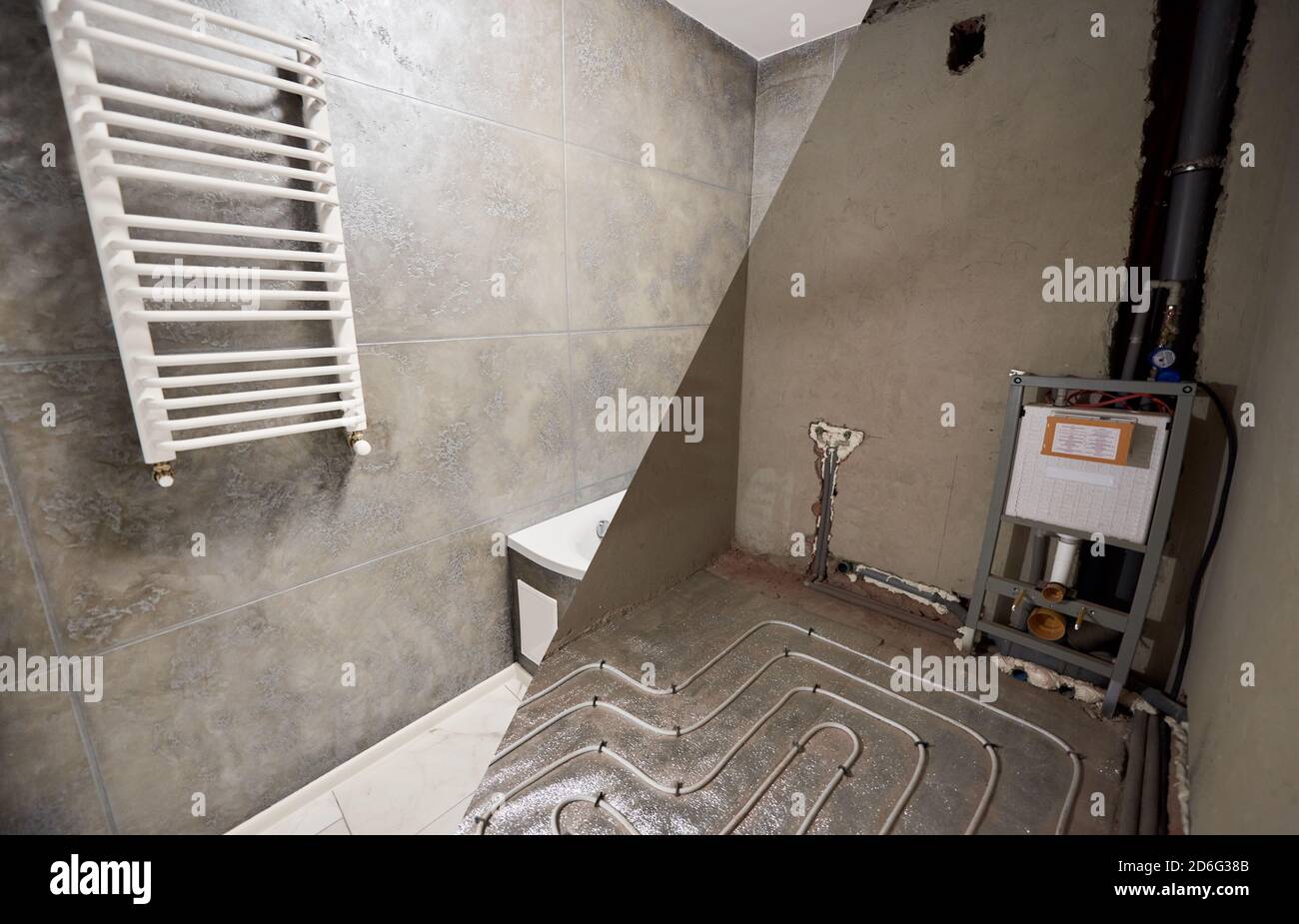 Comparative snapshot of bathroom in apartment before and after renovation. Grey plastering, ladder radiator hanging on wall, layer of heating pipes on the floor. Construction concept Stock Photo