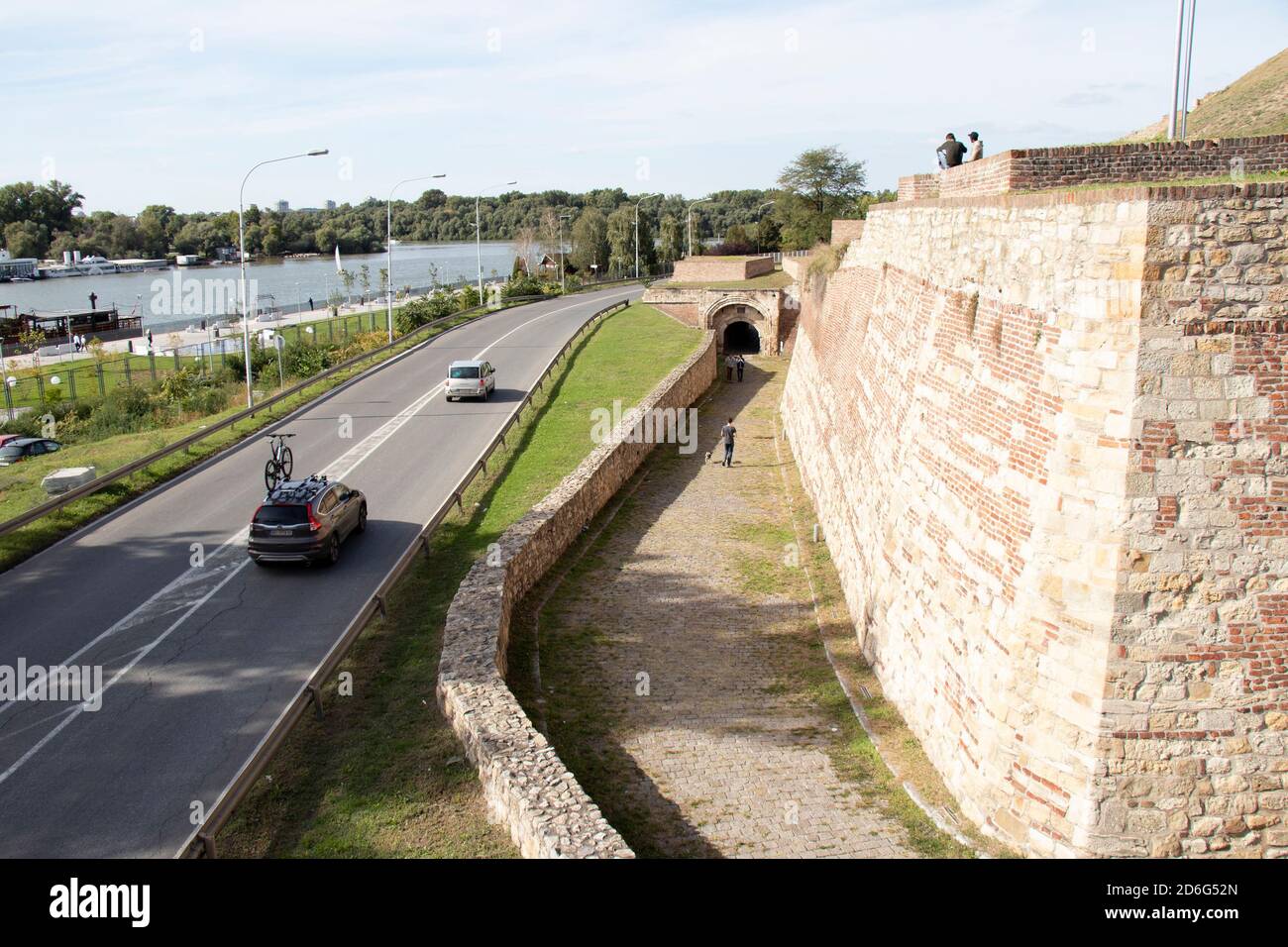 Belgrade, Serbia - October 09, 2020: People sitting and walking on foot path of fortress Kalemegdan, cars passing by on the street and the river water Stock Photo