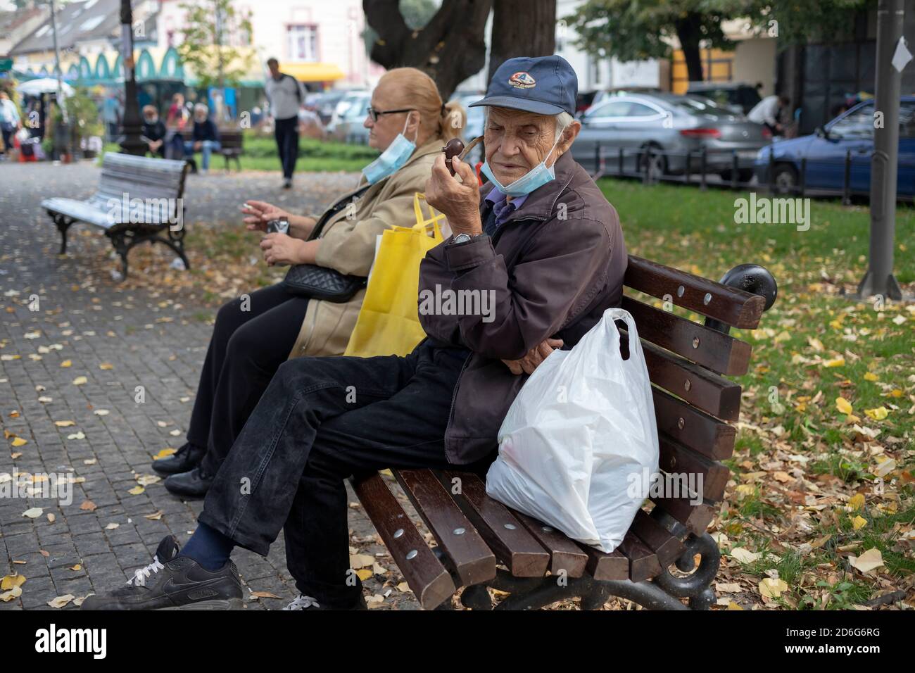 Belgrade, Serbia, Oct 11, 2020: Woman seated on a bench smoking cigarette next to a man smoking pipe Stock Photo