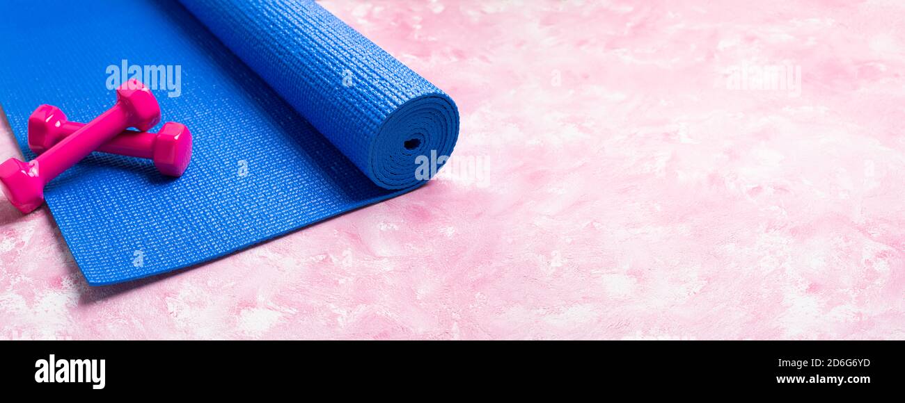 Blue yoga mat and dumbbells on pink background. Equipment for yoga, sport, fitness, workout. Concept healthy lifestyle, sport life, wellness. Long for Stock Photo