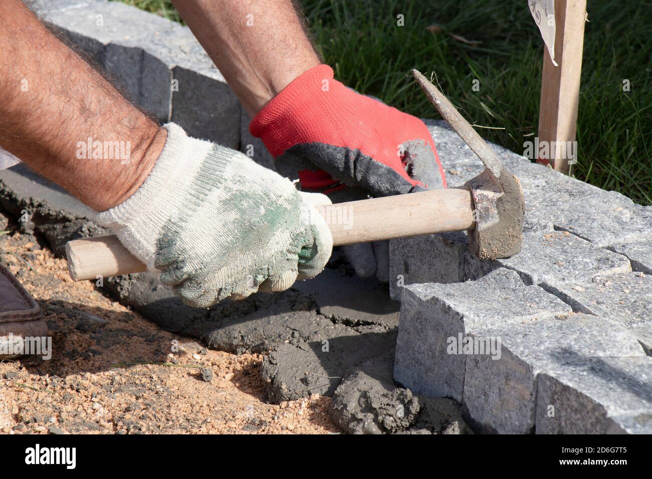 Hands in gloves of a builder worker laying on the granite cobblestone sett  on sand and mortar with hammer , paving  sidewalk Stock Photo