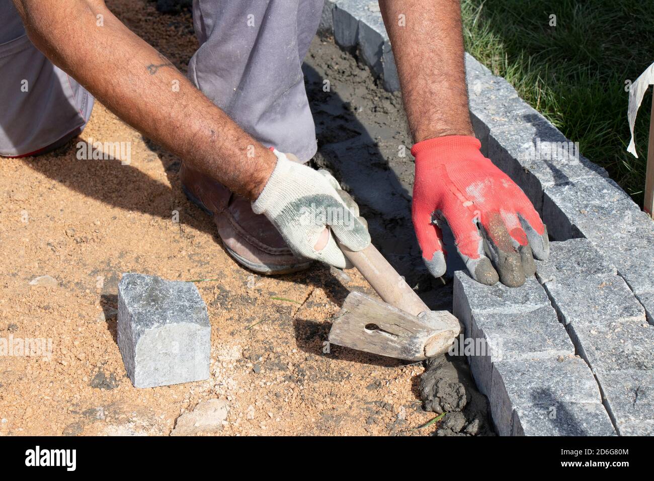 Hands in gloves of a builder worker laying on the granite cobblestone sett on sand and mortar with hammer , paving sidewalk Stock Photo