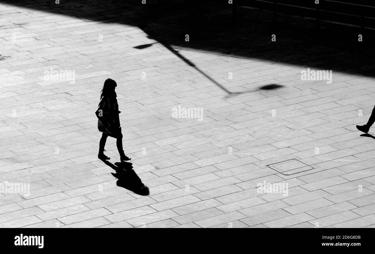 Belgrade, Serbia - October 09, 2020: Shadow silhouette of a young woman walking city square pavement, in high angle view black and white Stock Photo