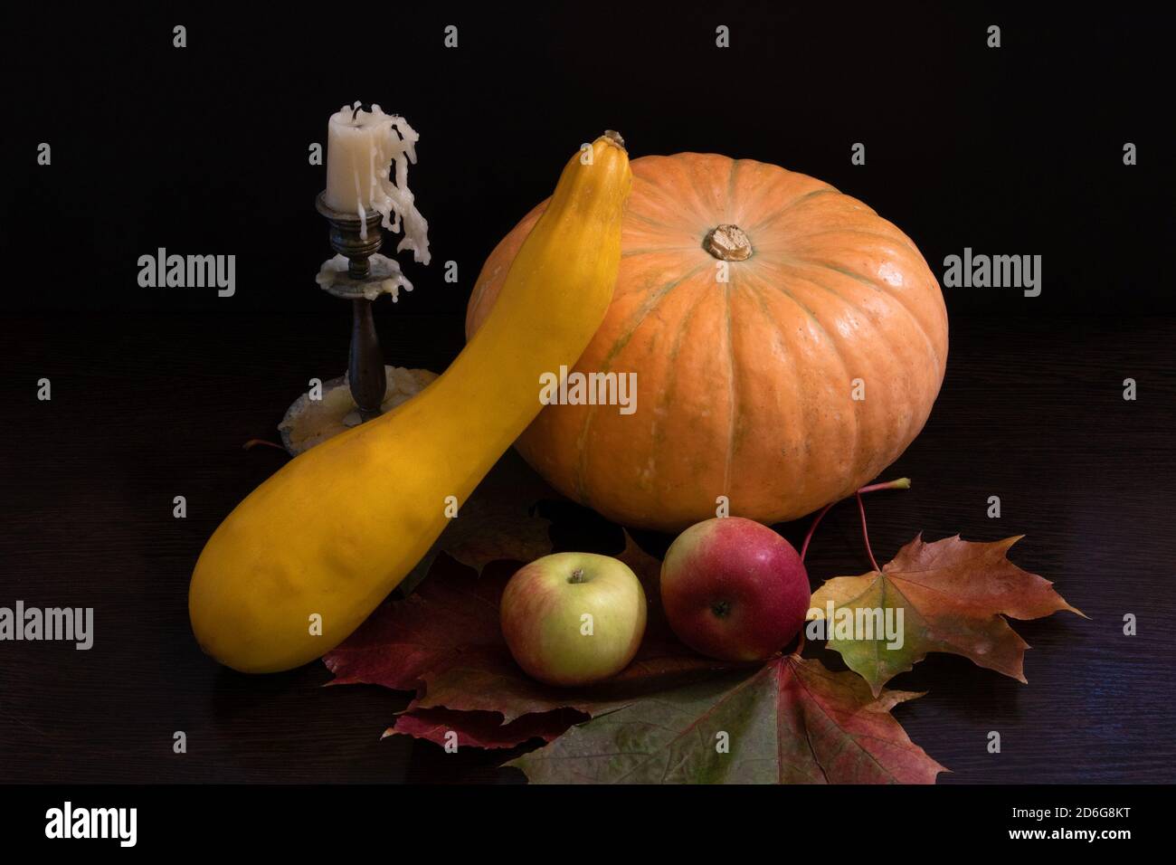 Autumn still life with big pumpkin, squash, apples and extinguished candle in bronze candlestick on the falling maple leaves Stock Photo