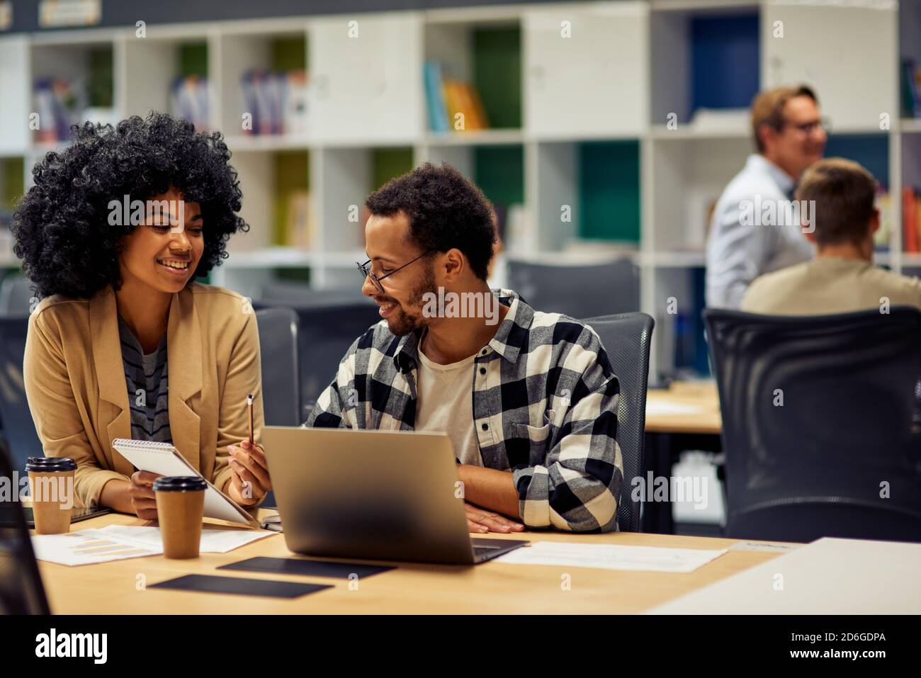 Two young diverse business colleagues discussing project, sharing fresh ideas while sitting at the desk and working together in coworking space. Office life, teamwork and business Stock Photo