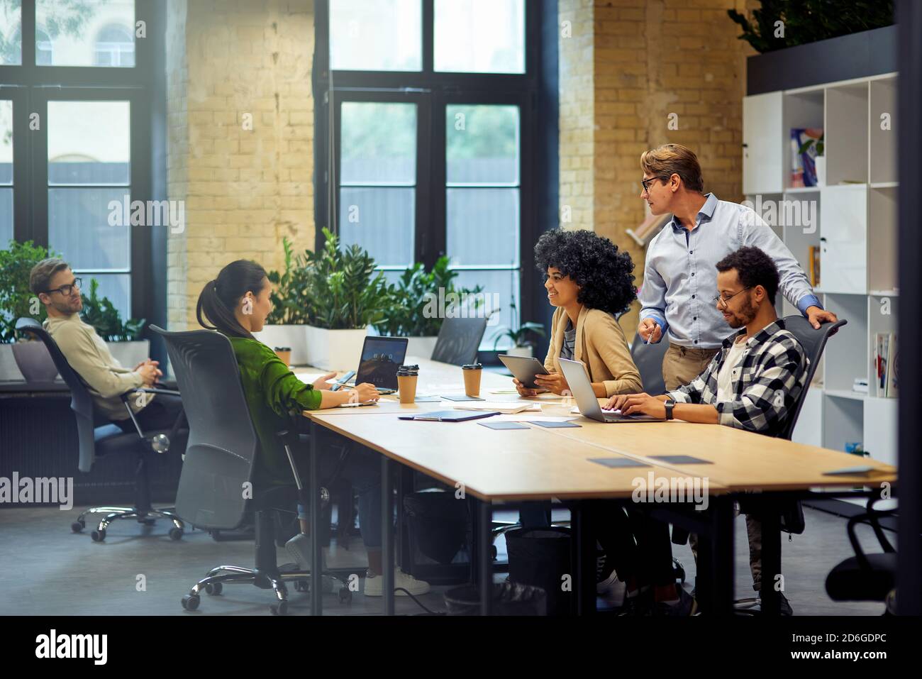 Office life. Group of young multiracial people sitting at the table in coworking space and working together, using modern technologies and discussing project. Business and teamwork concept Stock Photo