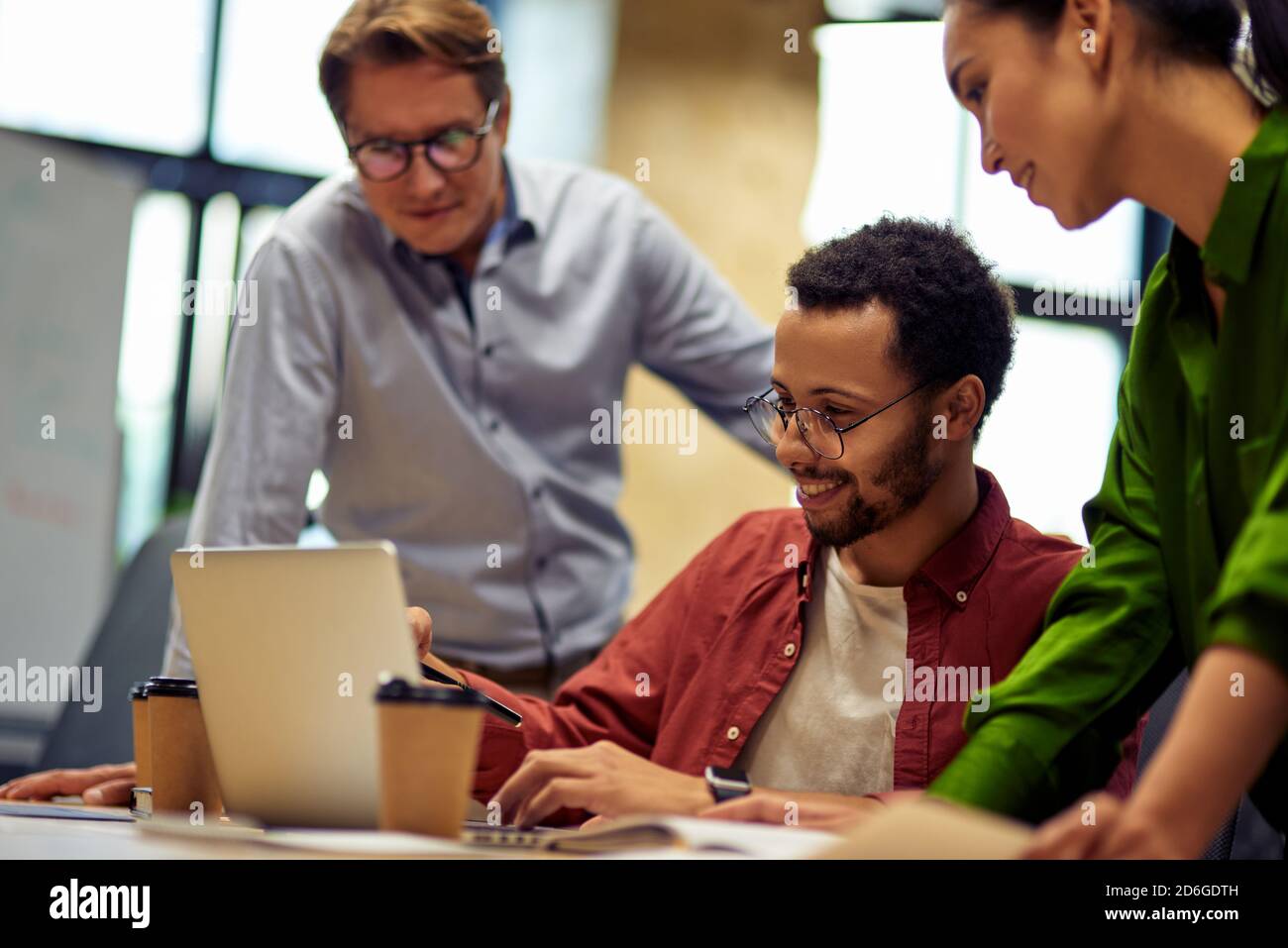 Successful project team. Group of focused multiracial business people looking at laptop screen and discussing work or project results while standing in the modern office or coworking space Stock Photo