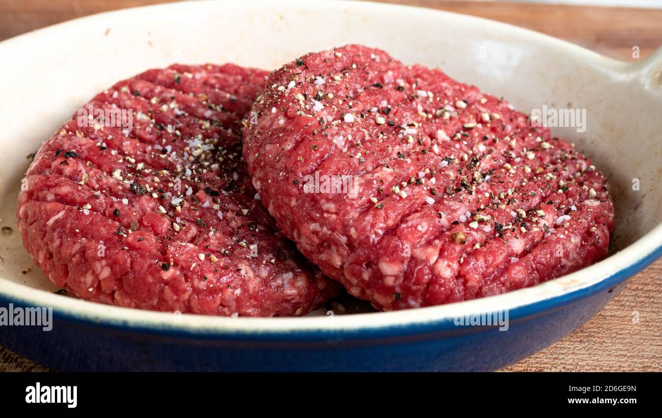 Two raw hamburger patties that are unseasoned, sitting outside in order to reach room temperature before putting them on the grill. Stock Photo