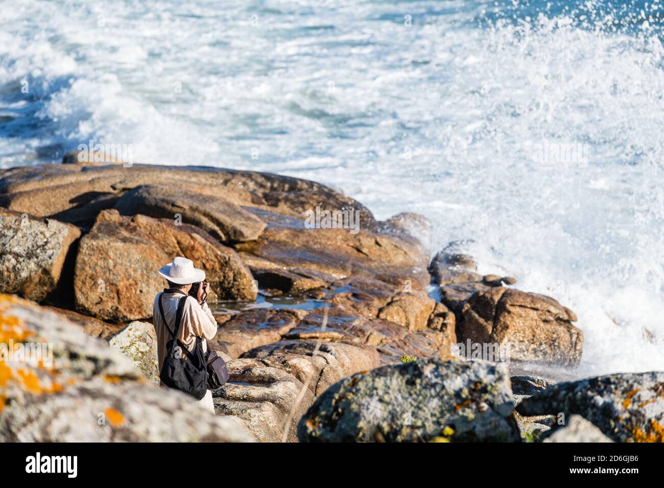 PORTONOVO, SPAIN - AUGUST 21, 2020: A well-equipped photographer takes pictures at sunset from the rocks in the Rias Baixas, Galicia. Stock Photo