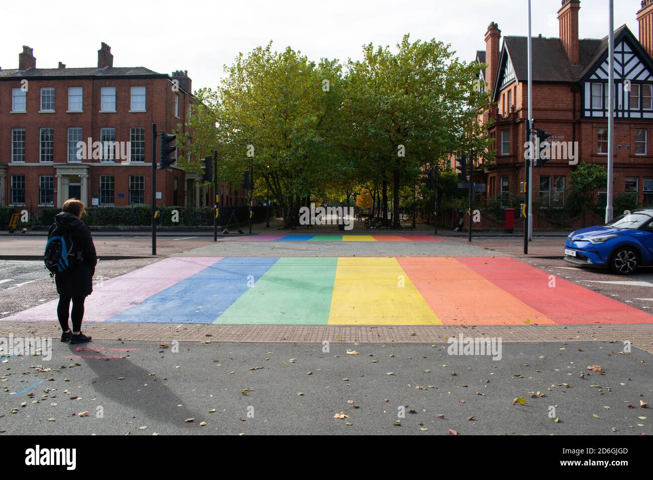 Pride rainbow crossing with woman waiting to cross and blue car on edge of design. Salford crescent speed hump. Salford University, UK Stock Photo