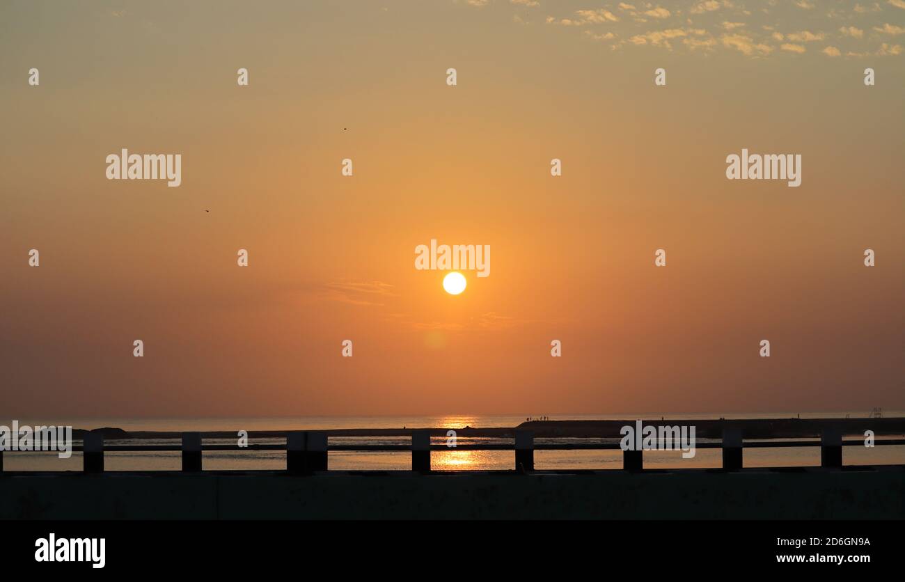 Beautiful landscape photography background with golden natural rays of the sun in the sky after sunrise from the ocean across the silhouette bridge Stock Photo
