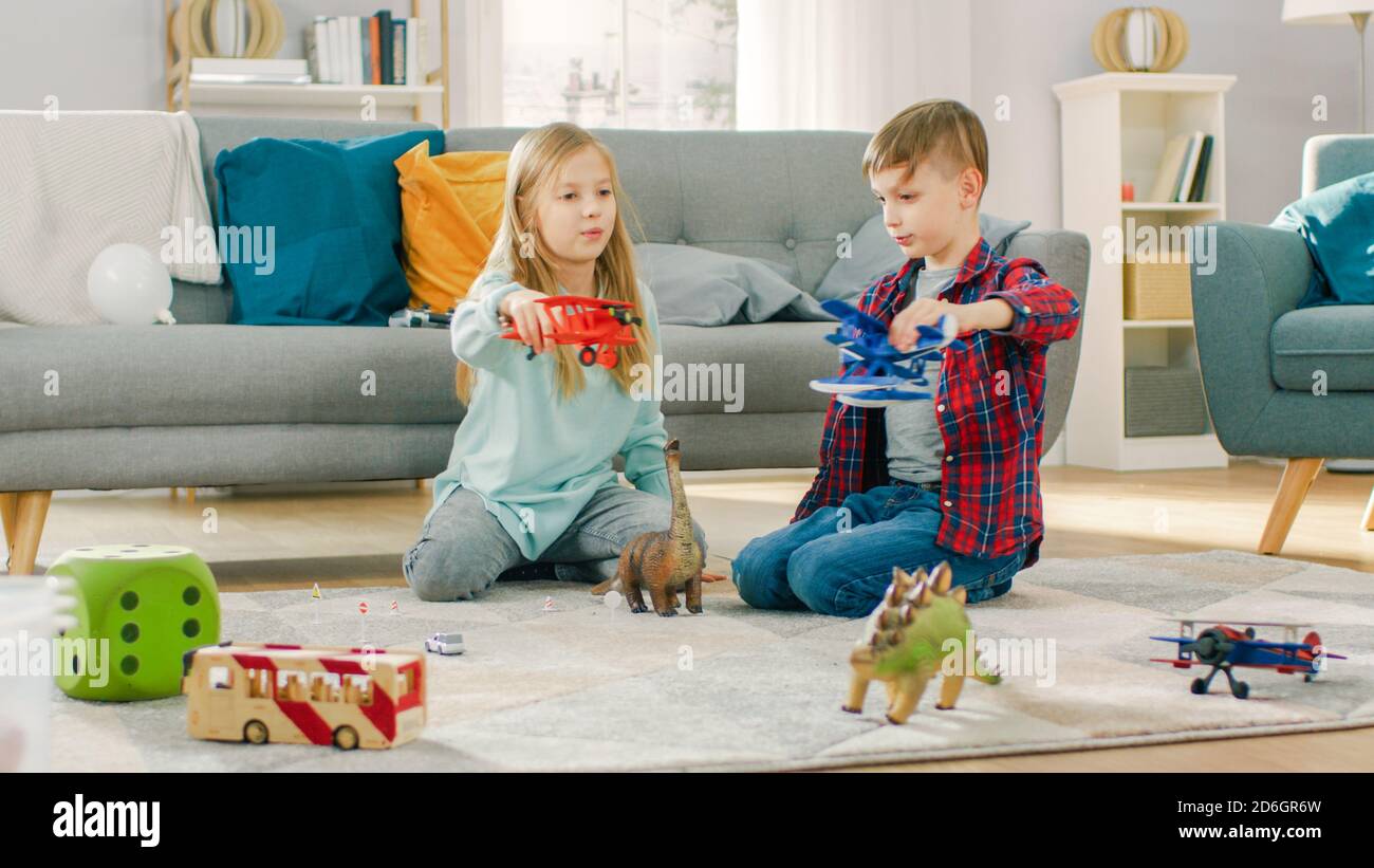 In the Living Room: Boy and Girl Playing with Toy Airplanes and Dinosaurs while Sitting on a Carpet. Sunny Living Room with Children Having Fun. Stock Photo